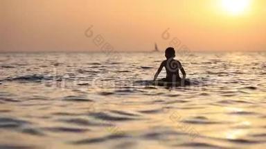 一个男孩<strong>漂浮</strong>在海面上的剪影，在<strong>橙色</strong>日落的极好背景上用冲浪板
